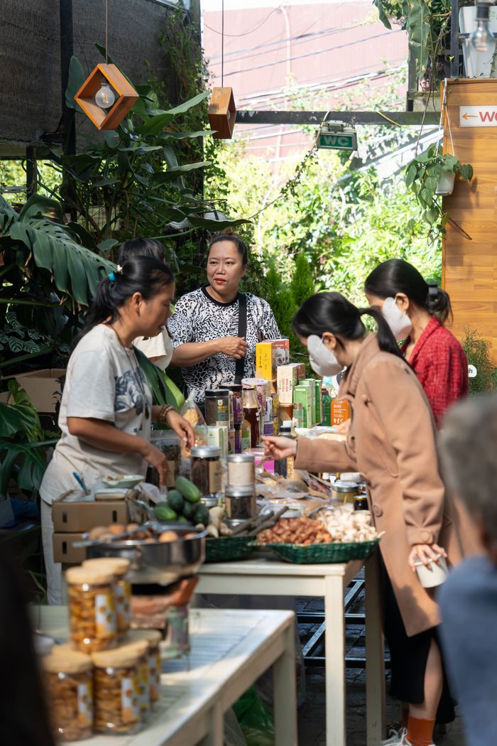 A vibrant indoor market scene with adults buying fresh produce and goods from vendors.