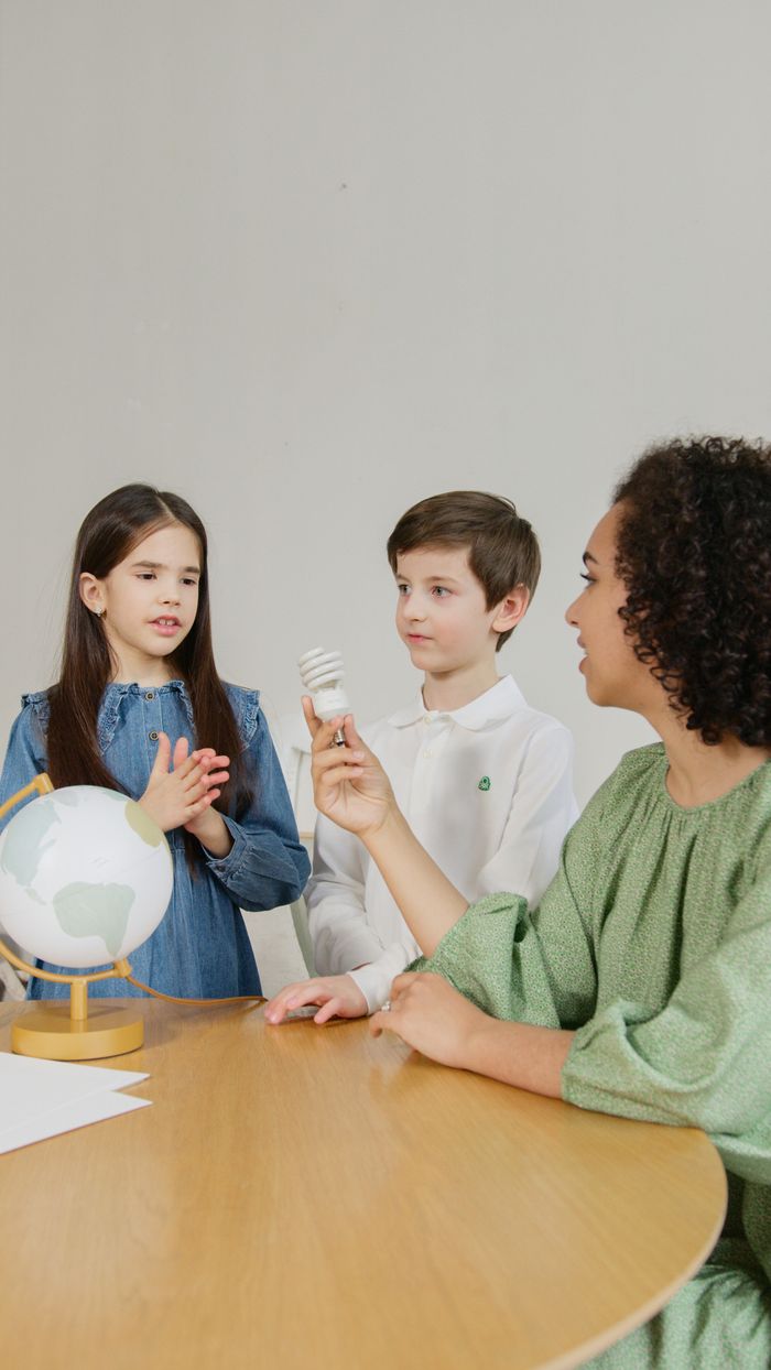 Teacher explains renewable energy concepts to children using a light bulb and globe.