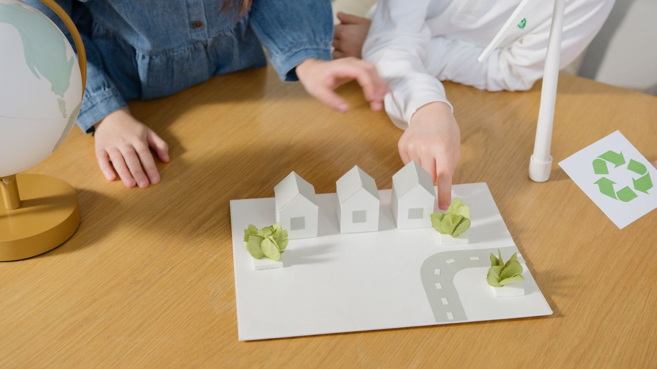 Children interacting with a paper model of eco-friendly houses, emphasizing sustainability.